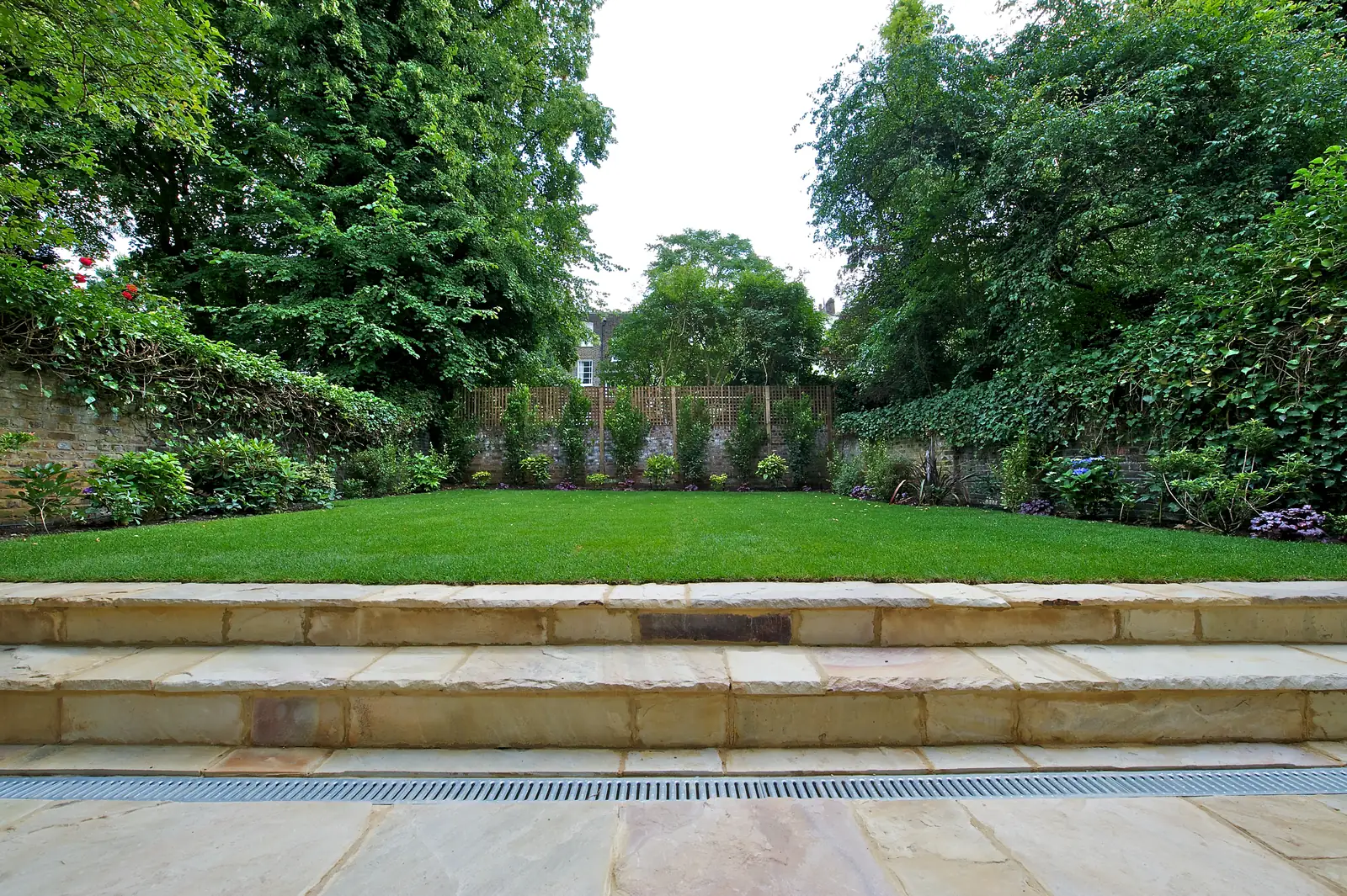 Rear garden after completion: new lawn, planted borders, trellis over the boundary wall and sandstone steps in the foreground