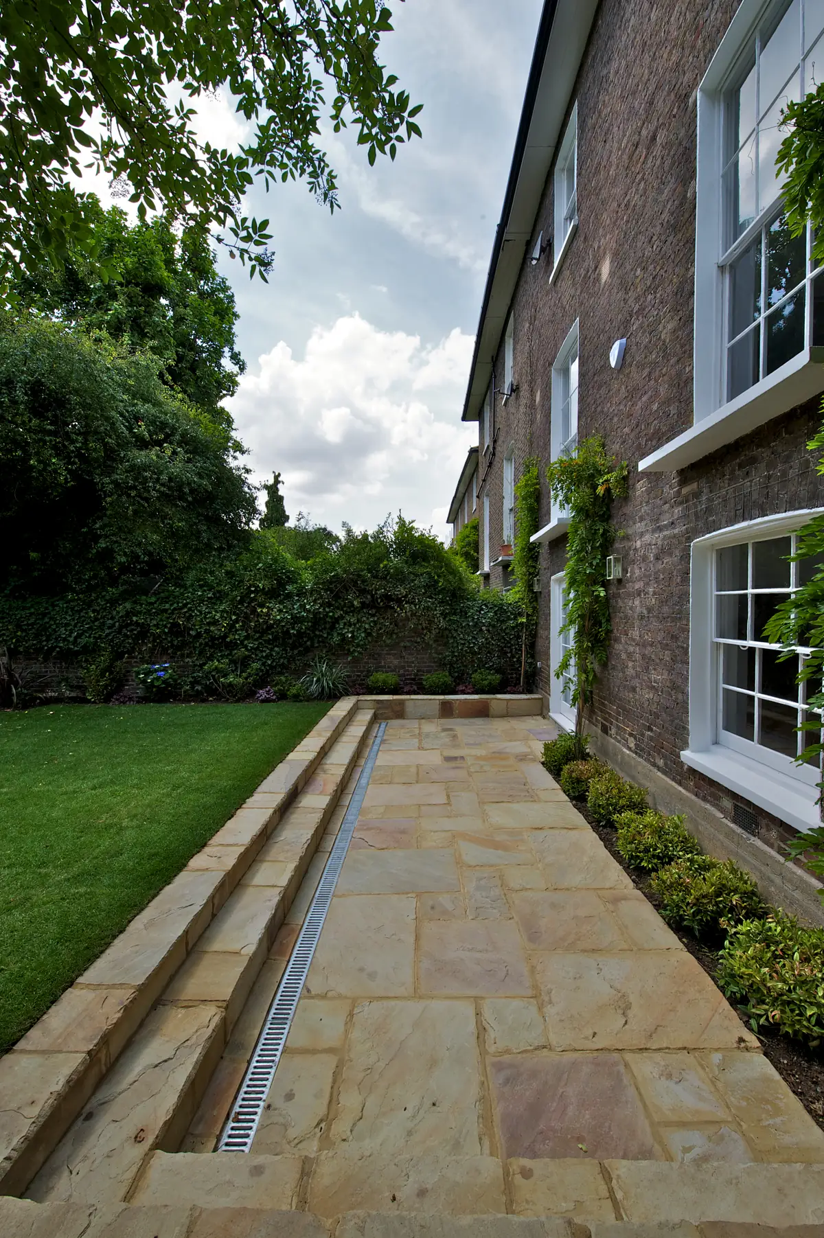 Sandstone paving along the side return with linear channel drainage and new planting against the house