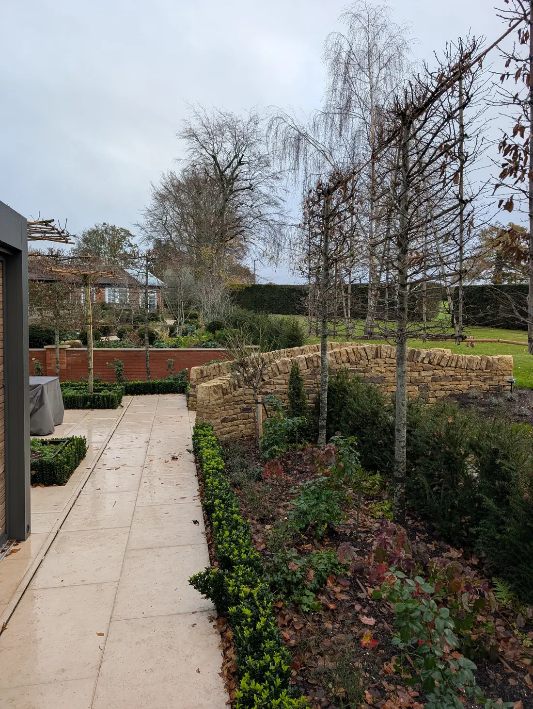 Bespoke dry stone walling flanking the garden transition, with pleached trees and box hedging