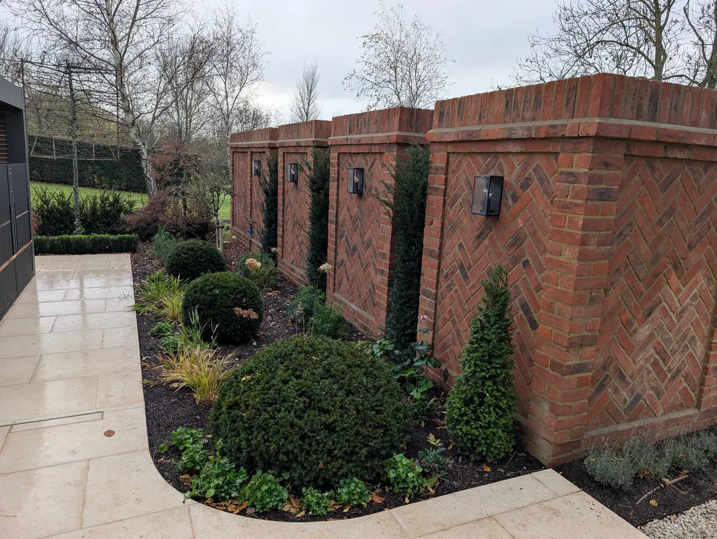 Feature brick walls in herringbone bond with integrated lanterns and yew planting