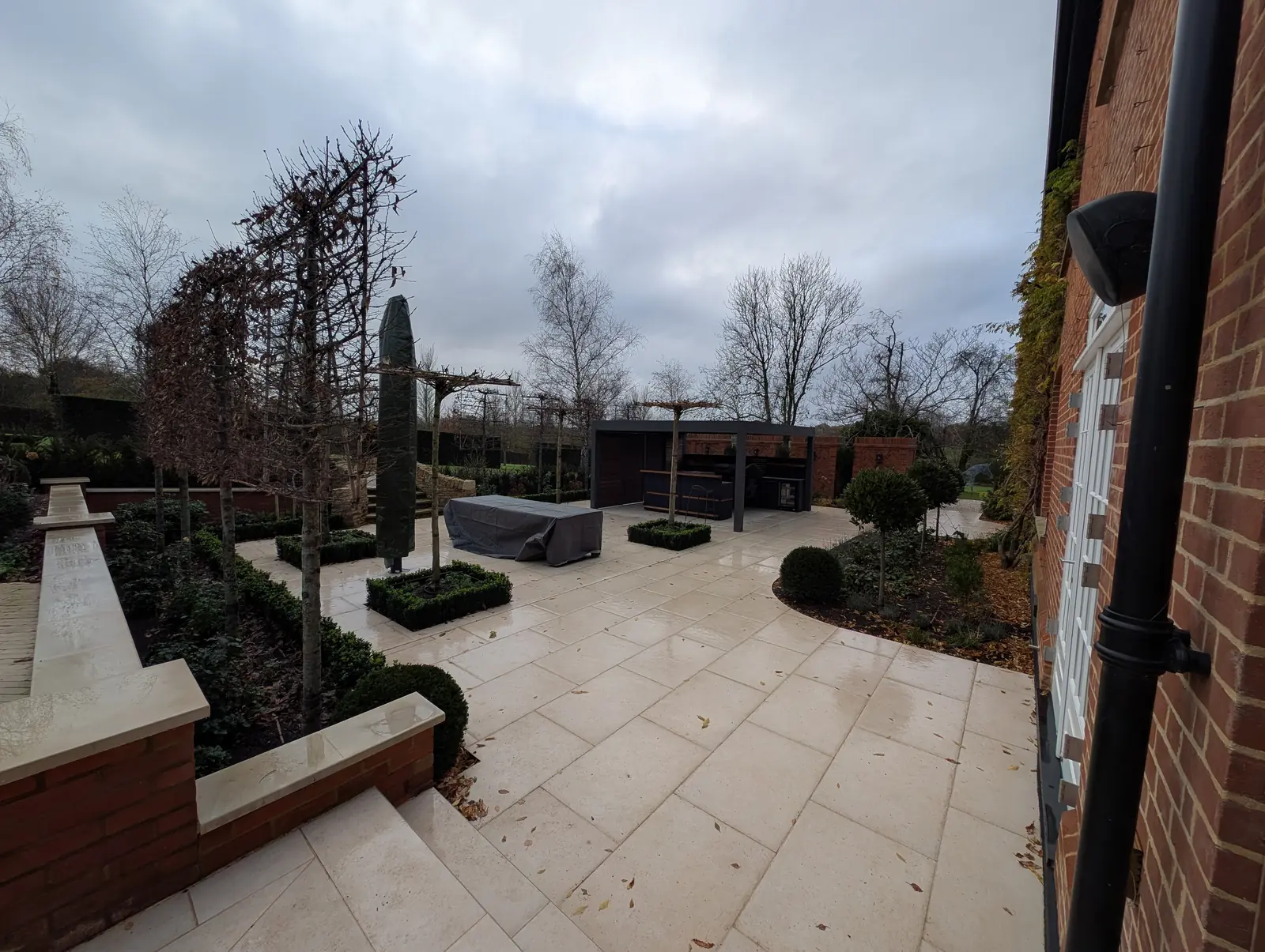 Completed 650 square metre landscaping project in St Albans: limestone terrace with box-edged pleached trees, feature brick walls and aluminium pergola